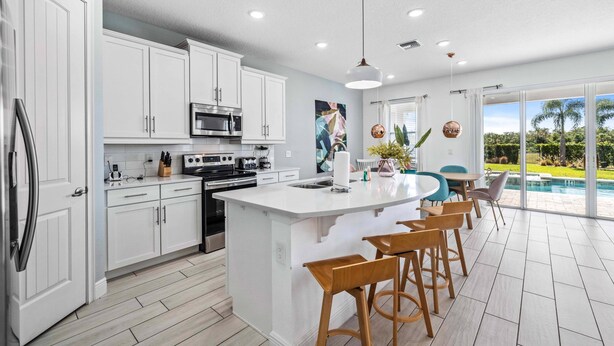 A modern kitchen with white cabinetry, a central island with bar stools, a large window overlooking a pool, and a ceiling fan. - Modern Family Villa Close To Disney With Private Pool (Kissimmee)