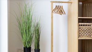 Une pièce avec une table ronde, deux plantes en pot, un porte-manteau en bois et un panier tressé.