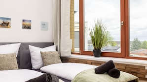 Une chambre d’hôtel avec une grande fenêtre, un lit avec une literie blanche et verte, une plante en pot sur le rebord de la fenêtre et trois tableaux encadrés accrochés au mur.