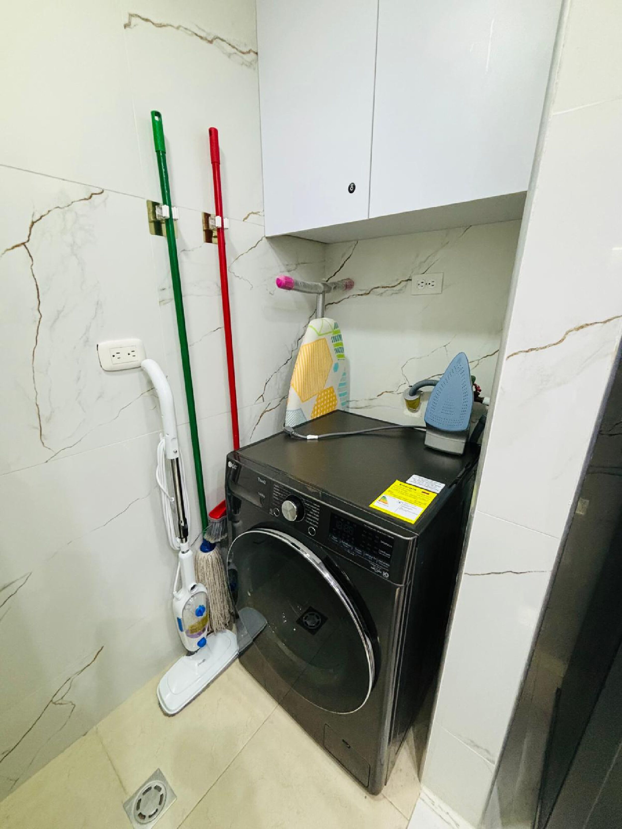 A compact laundry room with a washing machine, a mop, and a broom.