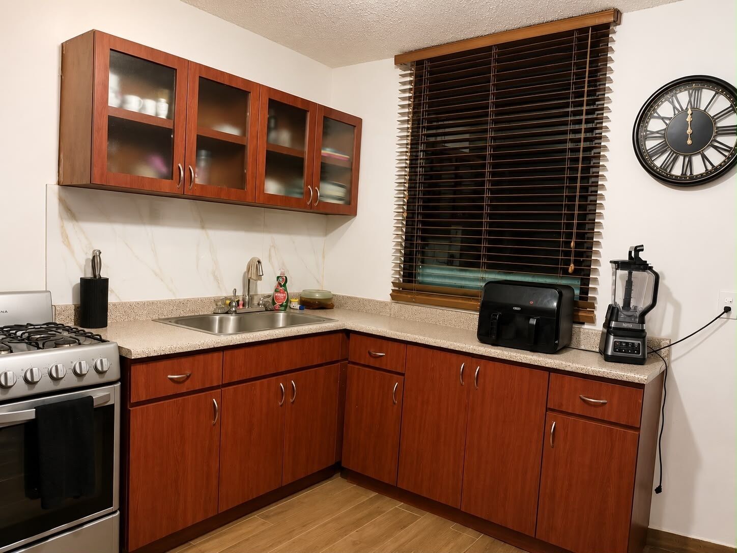 A kitchen with wooden cabinets, a stove, a sink, a toaster, and a blender.