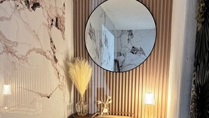 Un bagno angolare con parete in marmo, un mobile lavabo in legno con uno specchio e un portasciugamani.