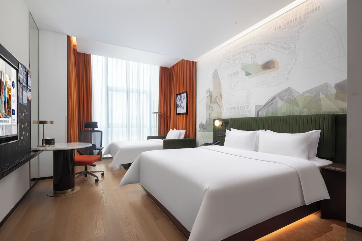 Une chambre d’hôtel avec deux lits, un bureau, une chaise et une grande fenêtre avec des rideaux.