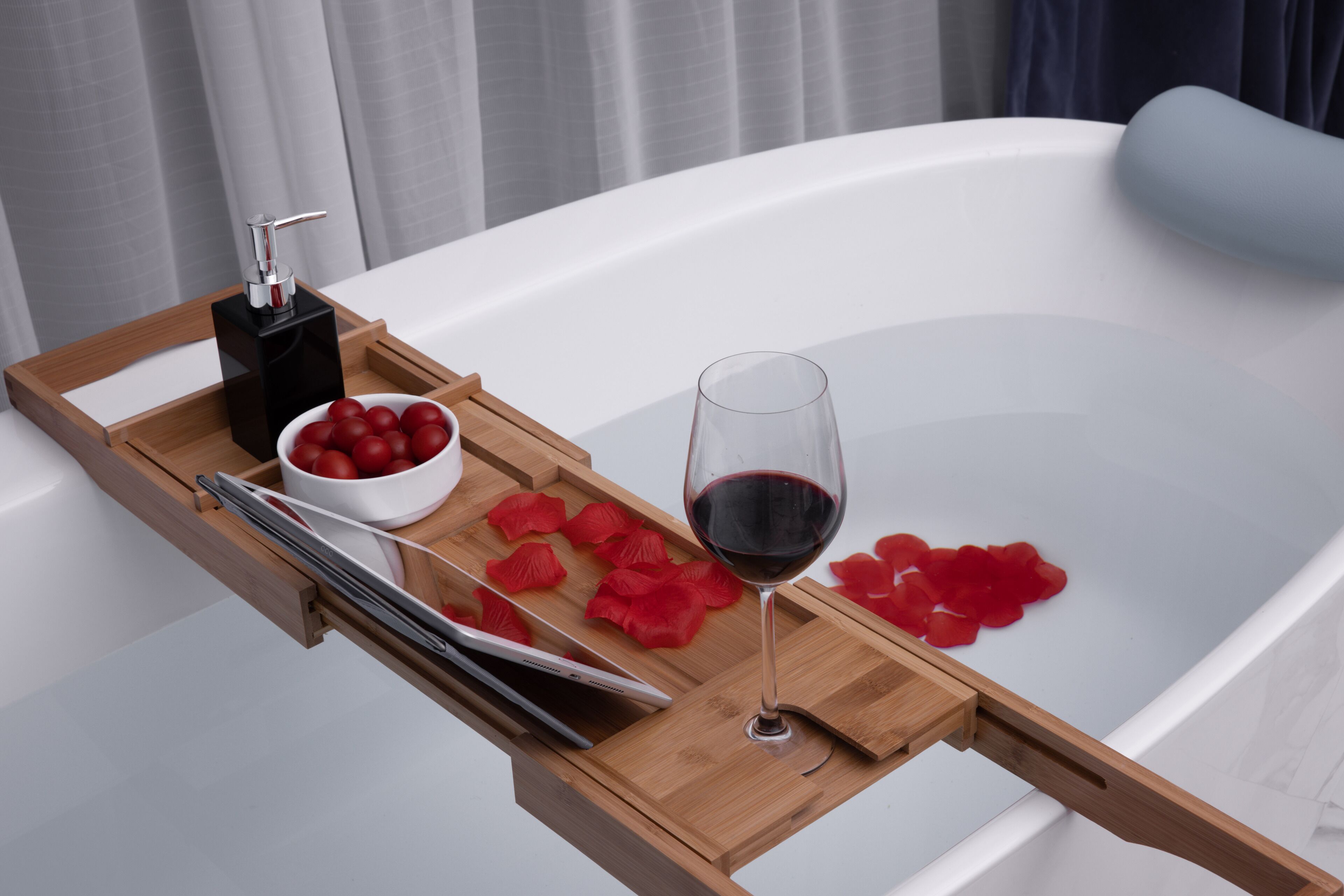 A bathtub with rose petals and a glass of red wine on a wooden tray.