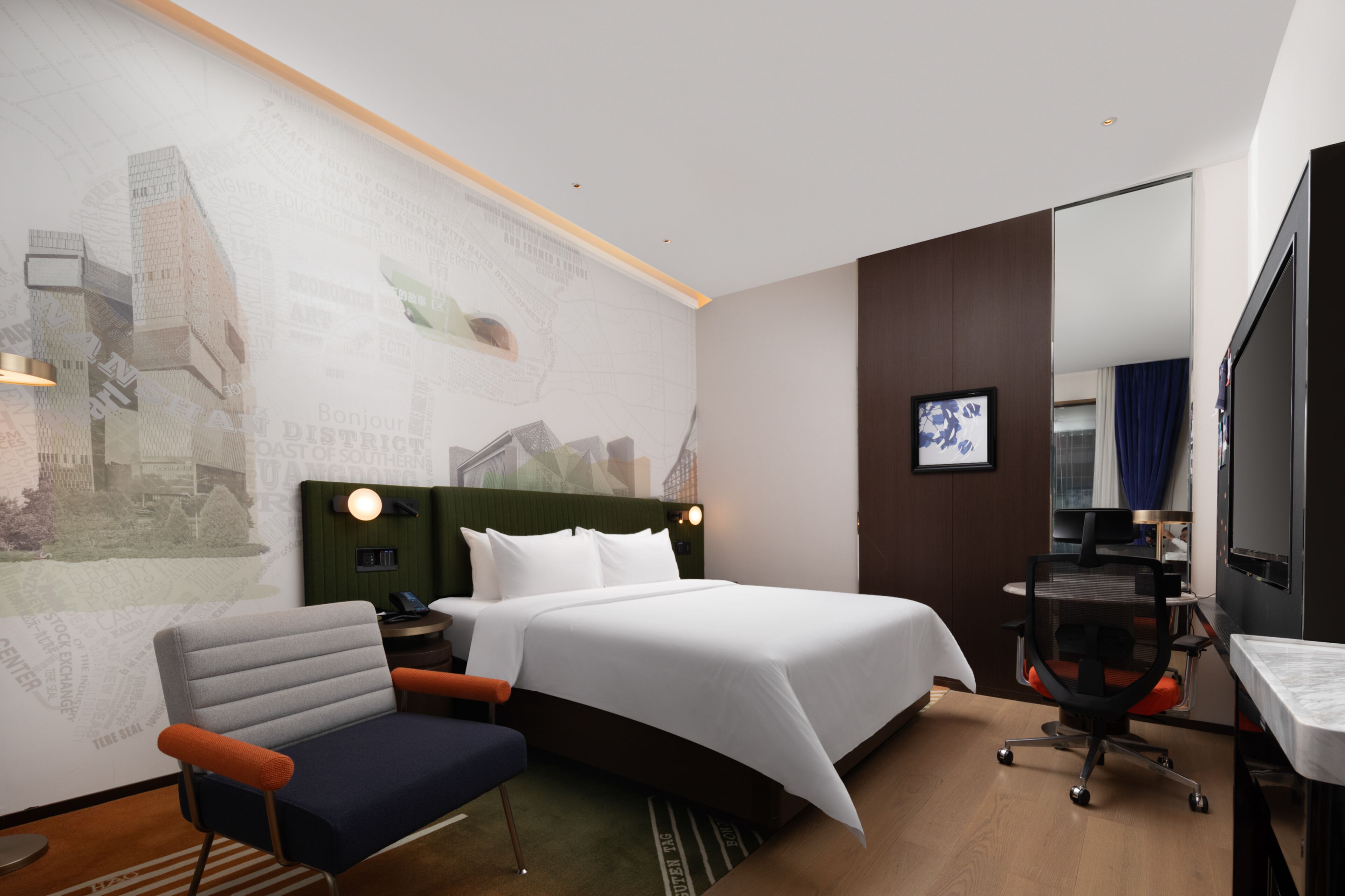 A hotel room with a bed, a desk, a chair, a TV, and a wall with a cityscape mural.