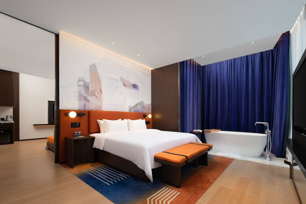 Une chambre d’hôtel moderne avec un grand lit, un banc, une baignoire et un téléviseur.