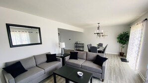 En moderne stue med en grå sofasæt, et sort sofabord og et spiseområde i baggrunden.