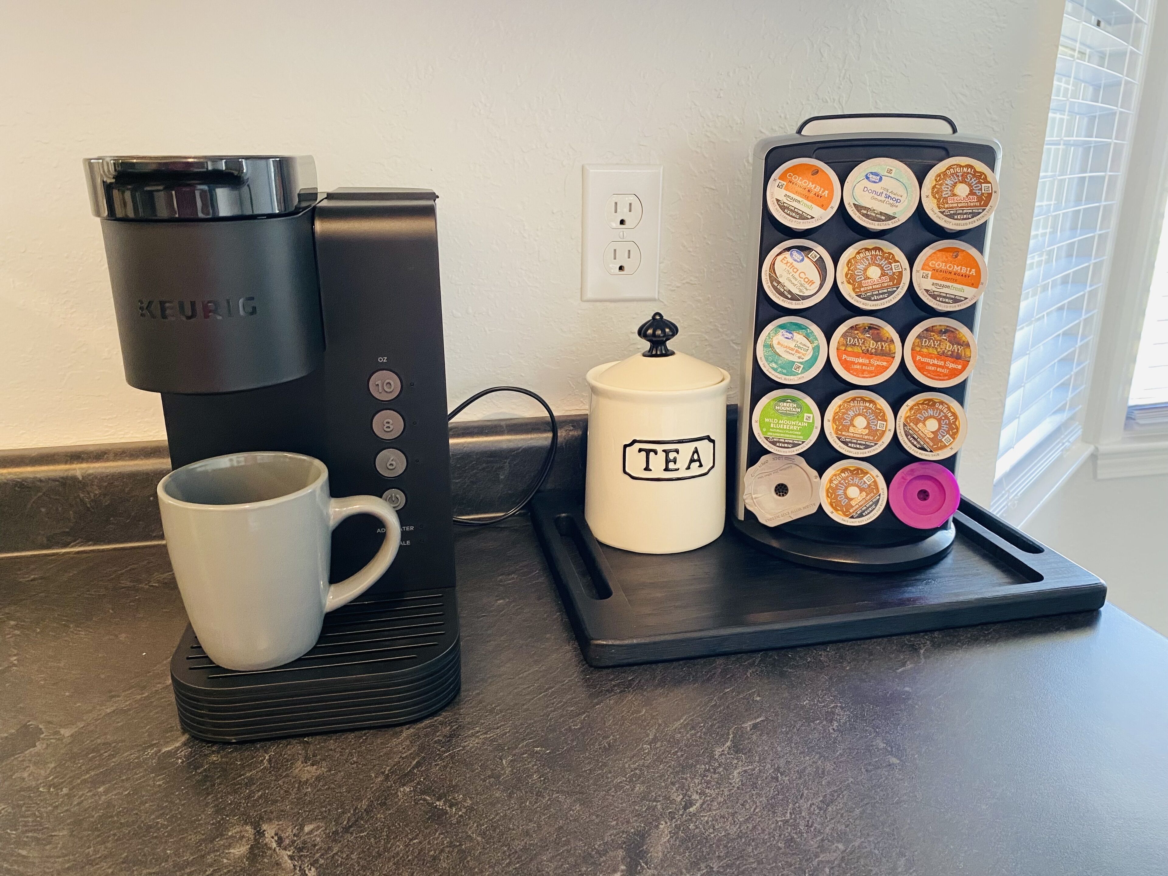 Een Keurig koffiezetapparaat, een mok en een theeketel met theefilter op een keukentafel.