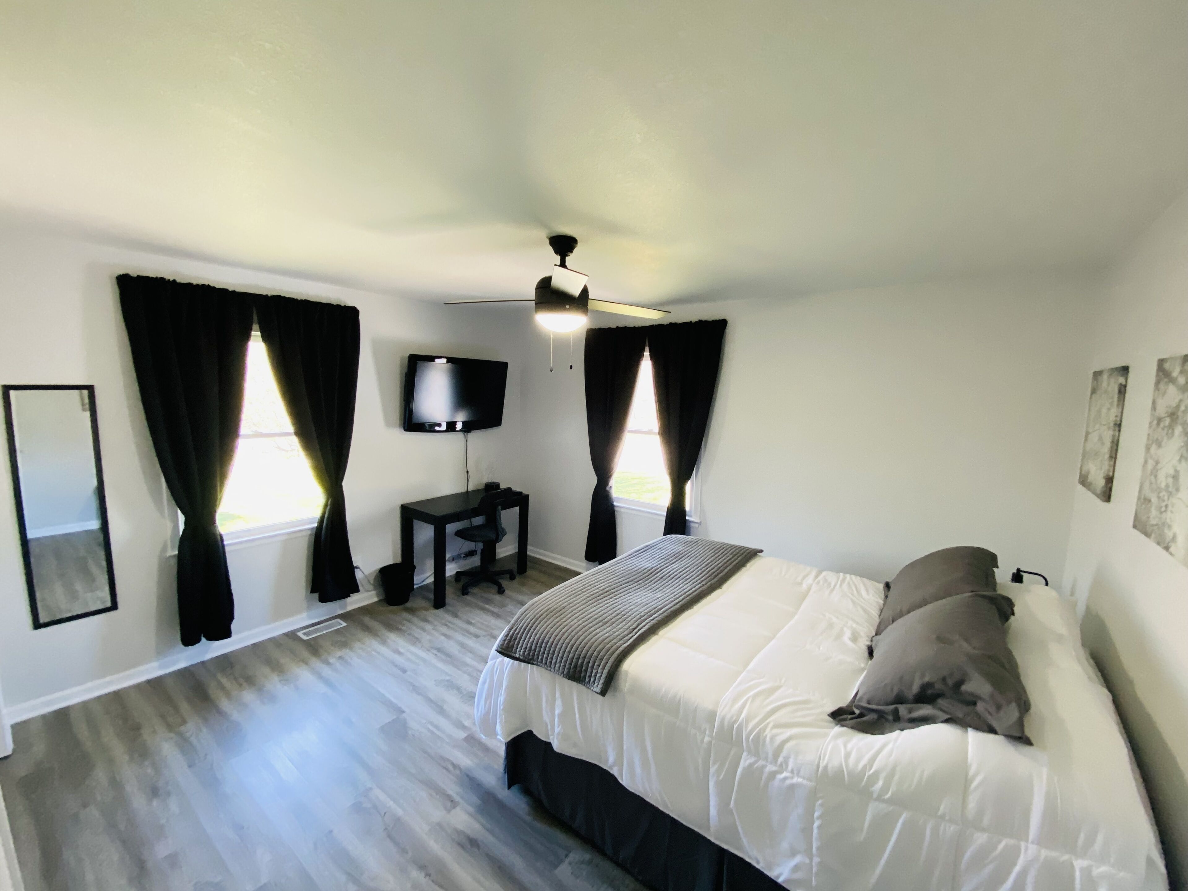 A bedroom with a bed, a desk, a TV, and a ceiling fan.