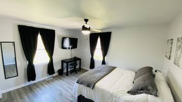 A bedroom with a bed, a desk, a TV, and a ceiling fan.