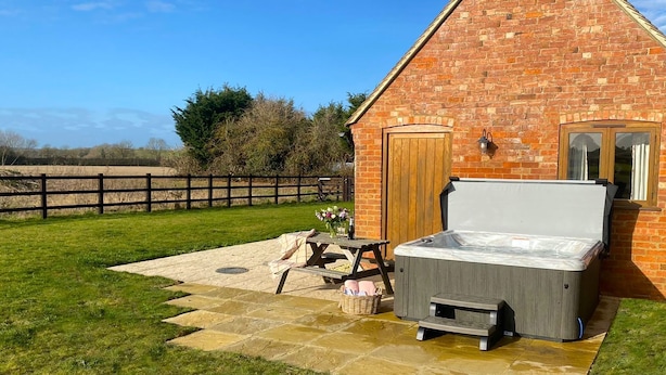 A brick building with a hot tub, a wooden door, and a small table with a vase of flowers.