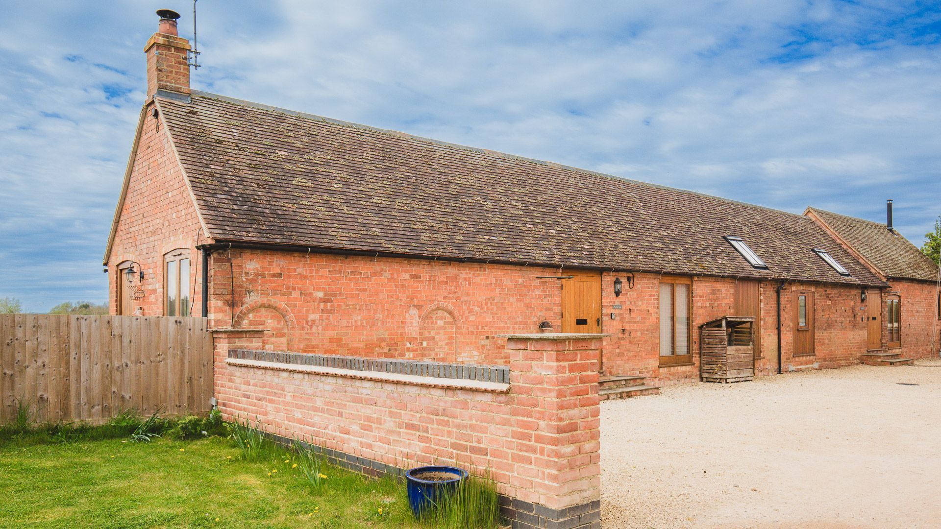 Un bâtiment en briques avec un toit en pente, une clôture en bois et une allée gravillonnée.