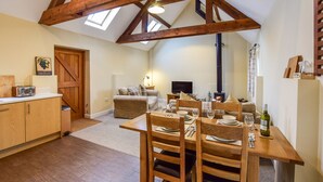 A cozy, rustic kitchen with wooden beams, a dining table set for four, and a fireplace in the background.