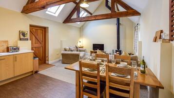 A cozy, rustic kitchen with wooden beams, a dining table set for four, and a fireplace in the background.