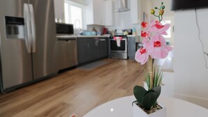 A modern kitchen with stainless steel appliances, a white countertop, and a potted orchid on a white table.