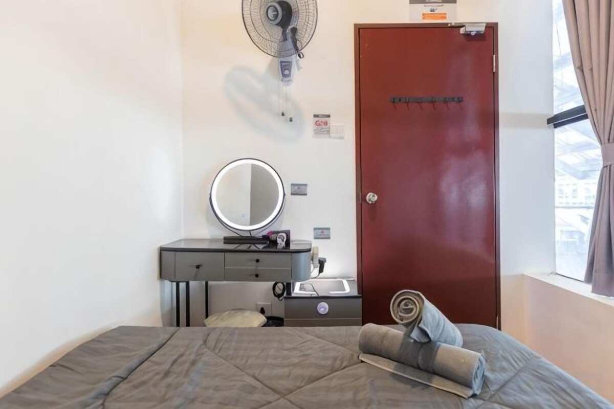 A bedroom with a bed, a dresser, a mirror, a fan, and a door.
