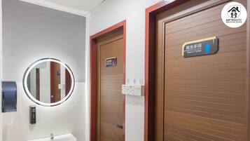 Baño de hombres con puerta de madera, espejo con luz y lavamanos.