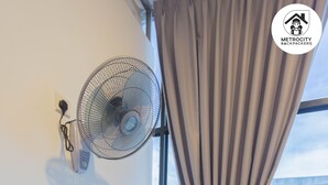 A modern room with a desk, a standing fan, a mirror, and a view of a parking lot through a large window. - MetroCity Backpackers (Kuching)