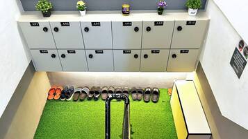 Un área para guardar zapatos con varios taquillones etiquetados de A01 a A10 y JR-A1, y una pequeña estantería con plantas en macetas.