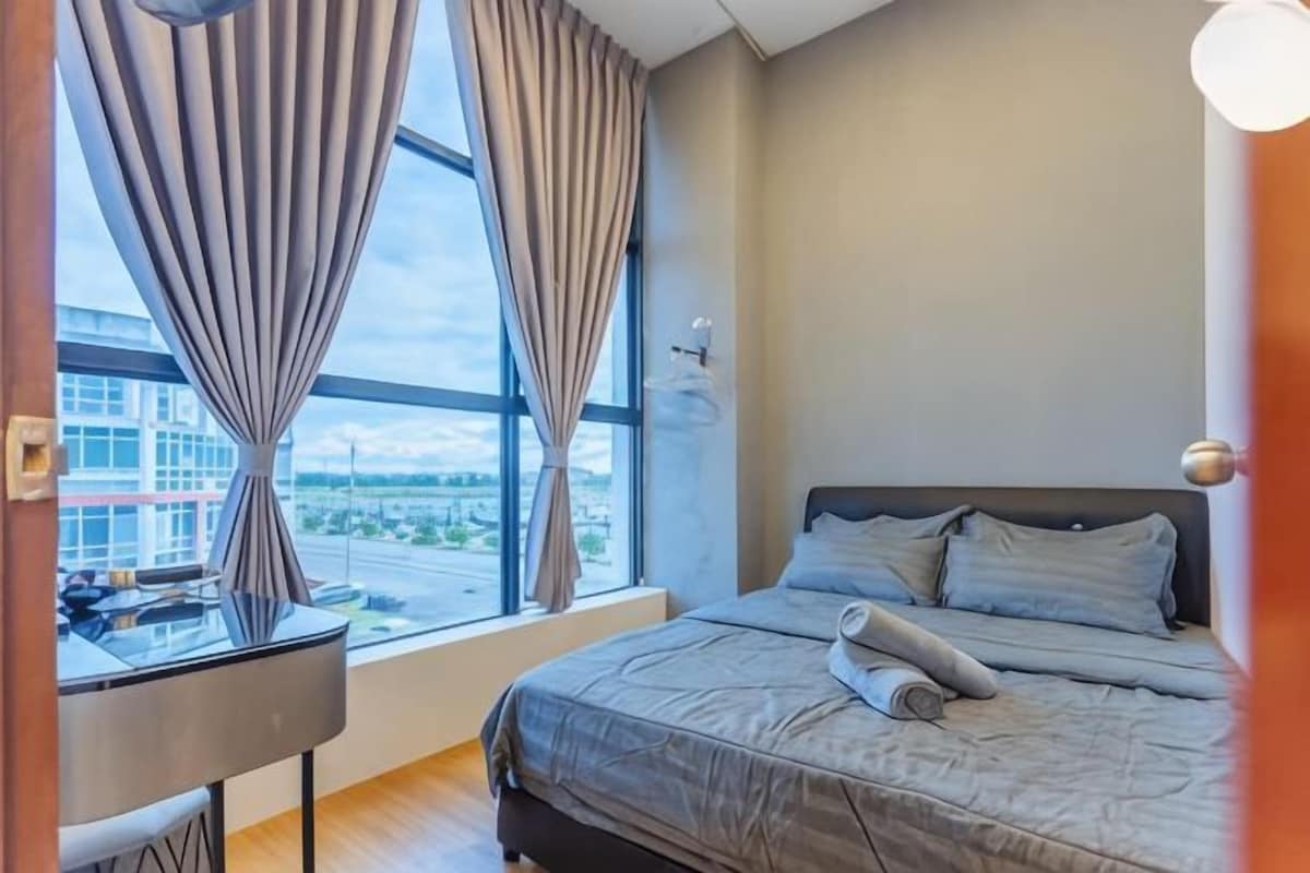 A hotel room with a bed, curtains, a desk, and a view of the outside.