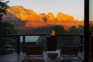 A deck with two lounge chairs and a fire feature, overlooking a canyon with rock formations.