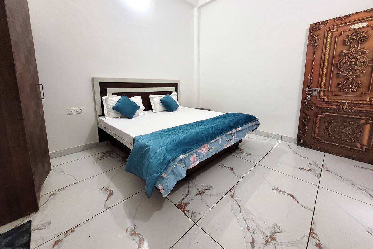 A bedroom with a bed, white walls, a wooden door, and a tiled floor.