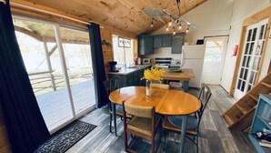 A wooden interior with a round dining table, chairs, a vase with yellow flowers, and a kitchen area with cabinets and appliances. - Willow Point Cabin:Brenchly Lake (Ulster)