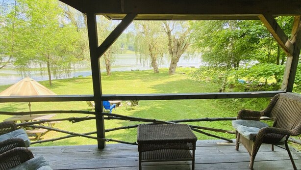 A covered outdoor seating area with wicker furniture, a view of a lake, and a grassy lawn. - Willow Point Cabin:Brenchly Lake (Ulster)