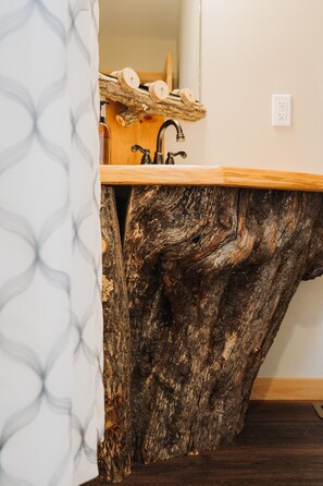 Un baño con un lavamanos original de tocón de árbol y una cortina de ducha con un diseño geométrico.