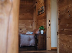Interior de una cabaña de madera con un sofá de cuero, una mesita con una planta y un cuadro en la pared.