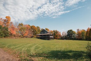 A rustic wooden house with a porch, surrounded by a grassy field and autumn-colored trees. - The Lodge by Towanda & Sayre PA (Ulster)