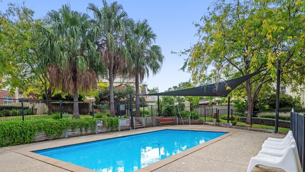 Piscina retangular com borda revestida, cercada por uma grade e protegida por um toldo.