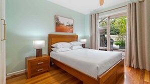 Quarto com cama de madeira, luminárias de cabeceira, ventilador de teto e vista para o exterior.