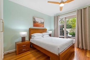 A bedroom with a wooden bed, bedside lamps, a ceiling fan, and a view of the outdoors. - Perfect 2-Bed Inner-City Home with Pool & BBQ Area (Clifton Hill)