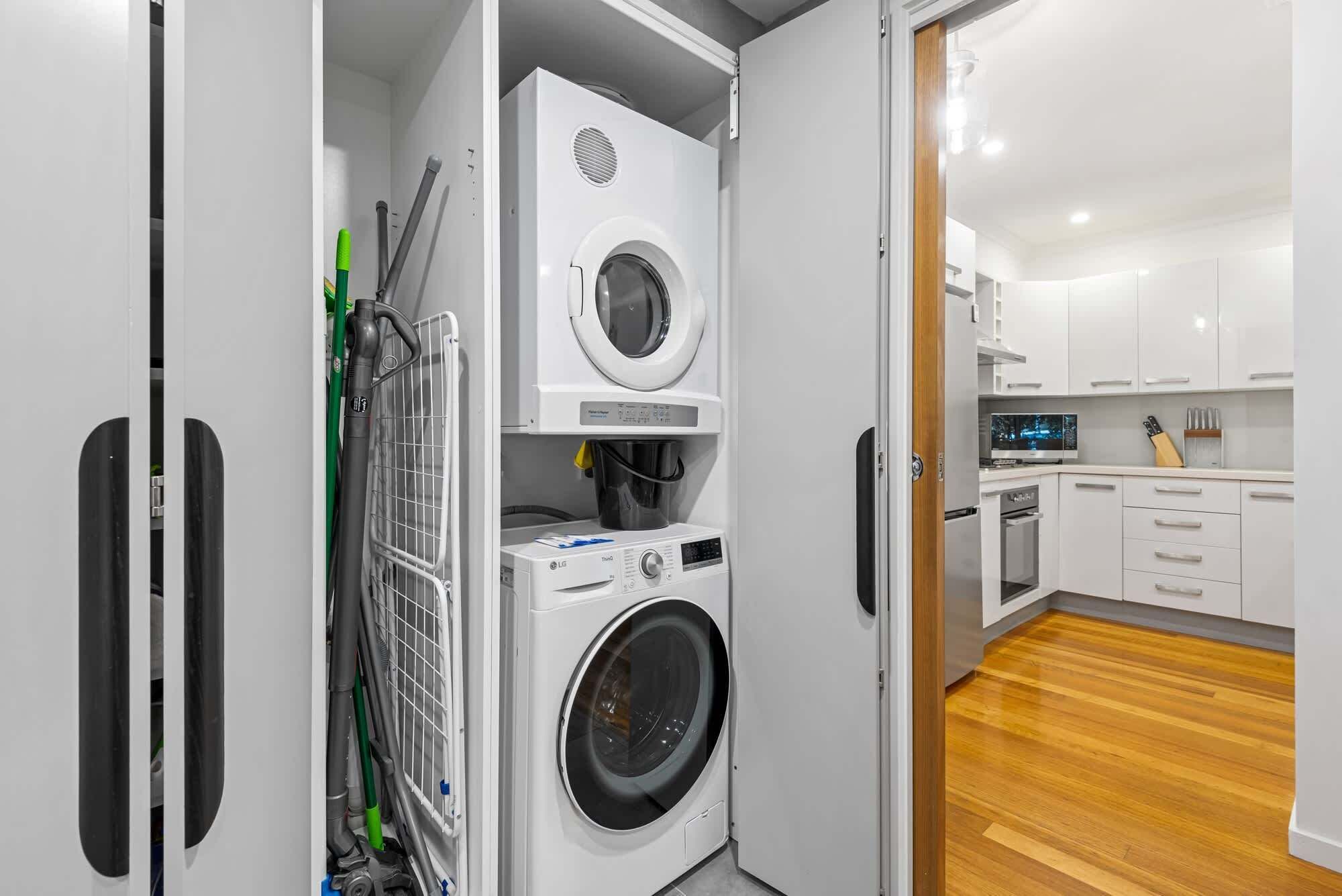 A compact laundry room with a washing machine, dryer, and a vacuum cleaner.
