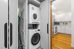 A compact laundry room with a washing machine, dryer, and a vacuum cleaner. - Perfect 2-Bed Inner-City Home with Pool & BBQ Area (Clifton Hill)