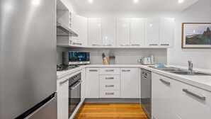 Uma cozinha moderna com armários brancos, piso de madeira, fogão, pia e um quadro na parede.