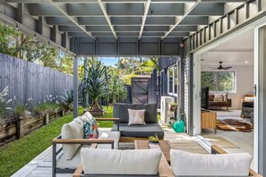 An outdoor living area with a sofa, chairs, and a table, connected to a modern interior space with a couch and a television. - Trendy 2-Bed Home with Outdoor Entertainment (Yaroomba)
