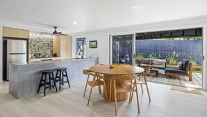 Een moderne keuken met een centraal eiland, barkrukken, en een eethoek met een ronde houten tafel en stoelen.