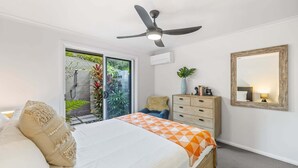 Een slaapkamer met een bed, een dressoir, een spiegel en een plafondventilator.
