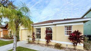 A residential house with a yellow facade, multiple windows with shutters, and a well-maintained lawn with various plants. - Fs3875ha - 4 Bedroom Villa In Sandy Ridge, Sleeps Up To 8, Just 6 Miles To Disney (Davenport)