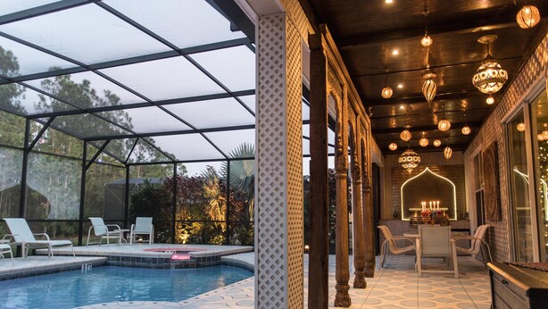 Un espace extérieur abrité avec une piscine, des chaises longues, un coin repas avec une table et des chaises, ainsi que des guirlandes lumineuses décoratives.