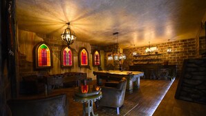 Eine Bar mit Holzboden, einer Billardkugel, Ledersesseln und farbigen Glasfenstern.