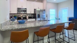 A modern kitchen with white cabinets, stainless steel appliances, a granite countertop, and four bar stools.
