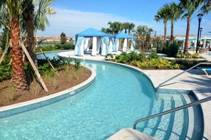 A pool area with a curved design, palm trees, and blue canopies. - Fs3998ha - 4 Bedroom Townhome In Windsor At Westside Resort, Sleeps Up To 8, Just 7 Miles To Disney (Kissimmee)