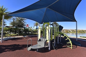 A playground with a climbing structure, slides, and a covered area with a blue canopy.