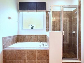 Une salle de bain avec une baignoire, une douche à parois de verre et une fenêtre avec un rideau.
