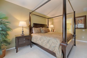 Een hemelbed met een donker houten frame en een bed met een patroon. Twee nachtkastjes met lampen en een potplant.