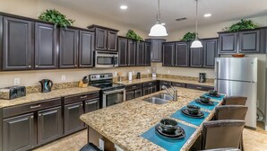 A modern kitchen with dark cabinets, granite countertops, stainless steel appliances, and a central island with seating. - It1020 - 6 Townhome in Paradise Cay, Sleeps Up To 12, Just 4 Miles To Disney (Kissimmee)