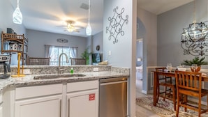 A modern kitchen with granite countertops, a built-in dishwasher, and a dining area with a wooden table and chairs. - It1072 - 3 Condo in Bahama Bay Resort, Sleeps Up To 6, Just 5 Miles To Disney (Davenport)